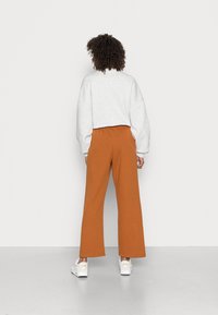 Szary, oversize'owy sweatshirt z opadającymi ramionami, w zestawieniu z pomarańczowymi spodniami o szerokich nogawkach. Model nosi białe trampki z logo.