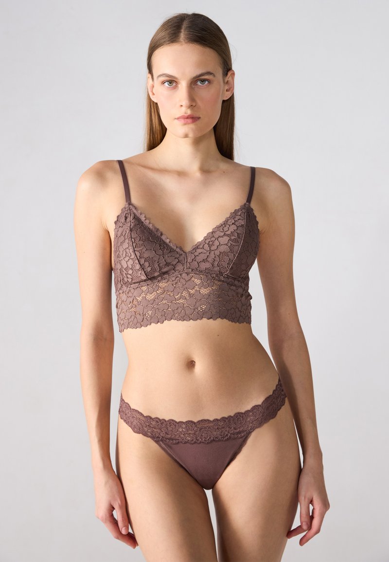 Ensemble en dentelle comprenant un bralette et un thong assorti, dans une couleur marron riche, avec des motifs floraux et des bords festonnés sur les deux pièces.