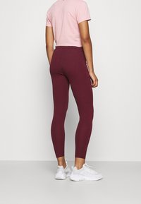 Leggings burdeos con una forma ajustada y una cintura elástica, combinados con una camiseta corta rosa y zapatillas deportivas blancas.