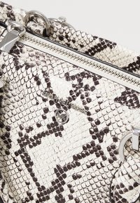 Gros plan sur un sac à main Michael Kors à motif peau de serpent blanc et noir avec une fermeture éclair argentée et un logo emblème.