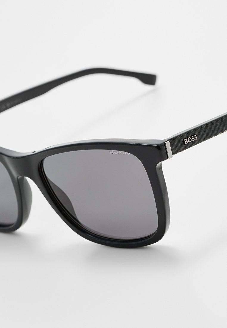 Schwarze polarisierte Sonnenbrille mit einem breiten quadratischen Rahmen, der an den Bügeln eine strukturierte silberne Verzierung und das Branding "BOSS" aufweist.