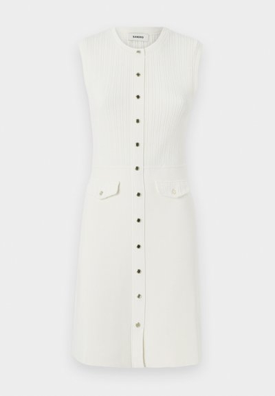 Robe blanche sans manches avec une texture côtelée, un col rond, des boutons sur le devant et deux poches poitrine avec des fermetures à bouton.