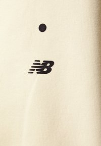 Tessuto di colore crema con una texture liscia, che presenta un dettaglio circolare nero sopra un logo "NB" nero. Design minimalista, senza motivi.