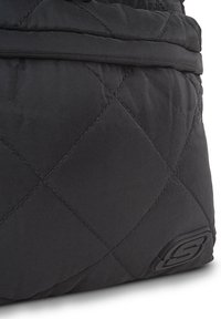 Mochila negra acolchada con un acabado suave, costuras prominentes y un acento de logo texturizado en la esquina inferior derecha.