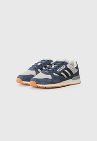 Sneakers bleumarin și gri din materiale din suede și textile, având trei dungi negre, un logo alb și o talpă din cauciuc de tip gum.
