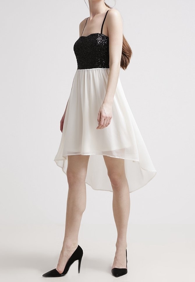 Zwart pailletten lijfje met dunne bandjes dat overgaat in een witte, vloeiende rok. Hoge-lage zoom en textuurstof. Zwarte hakken.