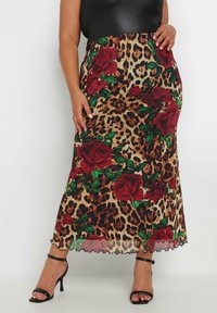 Falda maxi con estampado de leopardo y acentos en rosa rojo, textura transparente, cinturilla elástica negra y dobladillo con forma de ondas. Combinada con tacones negros de tiras.