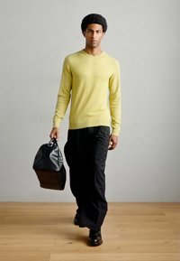 Κίτρινο πλεκτό πουλόβερ, μαύρο φαρδύ παντελόνι, κρατώντας μια υφασμάτινη μαύρη τσάντα με υφή. Ομαλό ύφασμα, άνετη εφαρμογή, απλός σχεδιασμός και μονόχρωμα χρώματα.