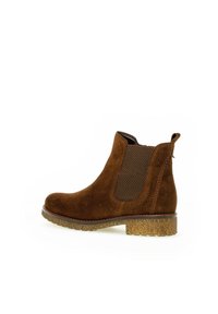 Stivaletto in suede marrone con pannelli laterali elastici, punta tonda e suola naturale texturizzata. Presenta un occhiello sul retro per facilitare l'indossamento.