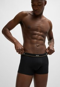 Zwarte boxershorts met een gestructureerde tailleband waarop "BOSS" in contrasterend wit is afgebeeld. De stof lijkt glad en sluit nauw aan.