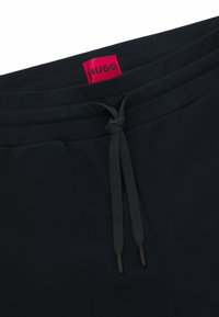 Svarta joggingsbyxor med elastisk midjeband, snörning och röd Hugo-logotyp. Mjukt tyg med en slät textur.