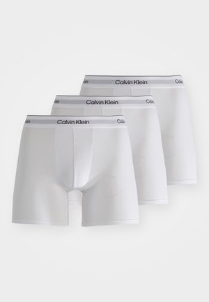 Trois paires de boxers blancs en coton avec une ceinture grise portant la marque "Calvin Klein" et un design classique et ajusté.