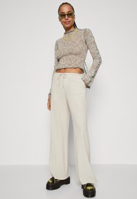 Stickad crop top i flerfärgat garn med vågiga kanter; krämfärgade vida byxor; kraftiga svarta plattformsskor med metalliska detaljer.