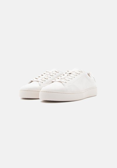 Λευκά δερμάτινα αθλητικά παπούτσια με στρογγυλεμένη μύτη, επίπεδη λαστιχένια σόλα και διακριτικές ραφές. Τα κορδόνια είναι στο ίδιο χρώμα.