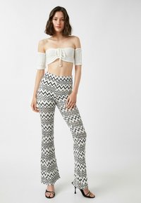Hvid cropped off-shoulder top med en frontknude; sort og hvid zigzag mønstrede flared bukser; sorte stropheels.
