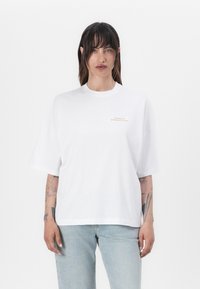 Bílé oversize tričko vyrobené z bavlny, s krátkými rukávy a kulatým výstřihem. Malé zlaté logo "Barbour International" na hrudi.
