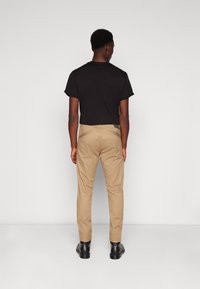 Moška črna majica s kratkimi rokavi, ujemajoča se s bež chino hlačami, z ozkim krojem in gladko teksturo, obuta v črne čevlje.