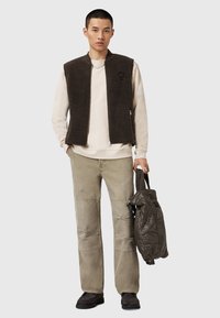 Dark brown sleeveless vest, beige sweatshirt, olive green pants, textured brown shoes, and a quilted gray bag. Casual layered outfit.