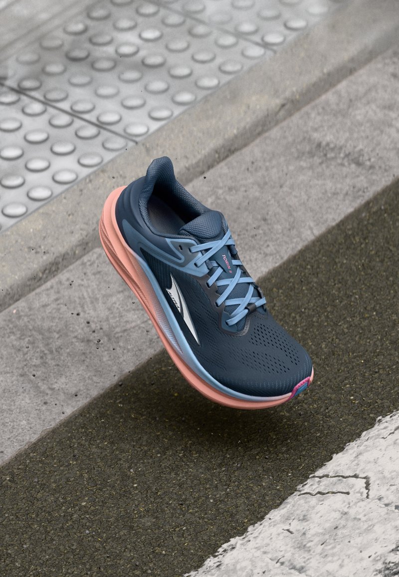 Baskets de course navy avec une tige respirante, accents bleu clair, semelle rose et surface texturée. Présente des lacets et un logo sur le côté.