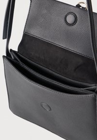 Μαύρη δερμάτινη τσάντα ώμου με καπάκι και μαγνητικό κούμπωμα, που δείχνει πολλαπλές εσωτερικές θήκες και ένα λείο εσωτερικό επένδυση από σουέντ.