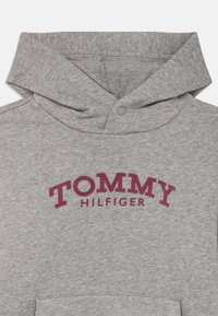 Γκρι φούτερ με κορδόνι και μπροστινή τσέπη, που διαθέτει την επιγραφή "TOMMY HILFIGER" σε μαρόν καμπύλη γραφή στο στήθος.