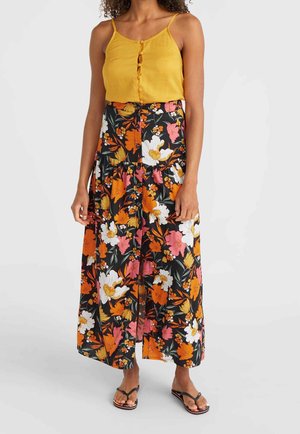Femme portant un haut sans manches jaune moutarde et une jupe noire taille haute boutonnée devant avec de grandes fleurs orange, blanches et roses.