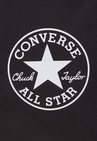 Schwarzer Stoffaufnäher mit einem weißen kreisförmigen Logo, das in der Mitte einen Stern hat. Der Text lautet "CONVERSE CHUCK TAYLOR ALL STAR."
