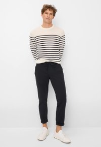 Crème en marine gestreepte trui gecombineerd met donkere joggerbroeken en witte sneakers. De trui heeft een ronde hals en ribbenboorden.