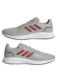 Paire de chaussures de running grises avec des rayures rouges, des semelles blanches et des semelles extérieures noires, vues de profil dans des directions opposées.