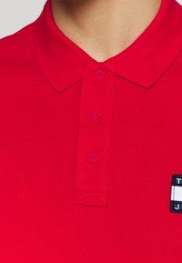 Rode polo shirt van textiel met een structuur, een drievoudige knoopsluiting en een klein logo op de linkerzijde. Eenvoudig en klassiek ontwerp.