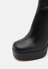 Black high-heeled boot made of smooth leather, featuring a rounded toe and a chunky platform sole for added height and stability.