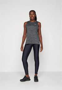 Gray athletic tank top with a round neckline, paired with dark leggings and black sneakers, standing on a neutral background.