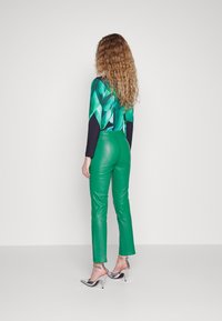 Gröna läderbyxor med en slät yta, matchade med en topp med flerfärgad geometrisk design i nyanser av grönt och mörkblått. Silverklackar.