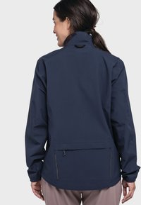 Marineblauer wasserdichter Mantel mit langen Ärmeln, hohem Kragen und seitlichen Reißverschlusstaschen. Verfügt über einen verstellbaren Kordelzug am Saum für eine anpassbare Passform.