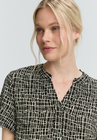 Chemise noire et blanche à manches courtes avec un motif à carreaux, dotée d'un col en V et d'une texture de tissu douce.