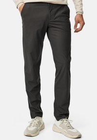Pantalons slim-fit gris foncé en tissu lisse, dotés de poches latérales et d'une taille élastique ; associés à des baskets de couleur claire.