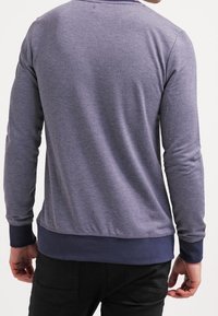 Felpa grigia a maniche lunghe con scollo rotondo, caratterizzata da polsini e vita in contrasto di colore blu navy. Texture liscia, design aderente e dettagli minimi.