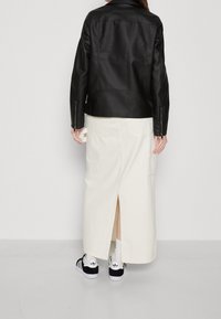 Czarna skórzana kurtka o wyrazistej konstrukcji, połączona z kremową maxi spódnicą z bocznym rozcięciem oraz czarno-białymi sneakersami.