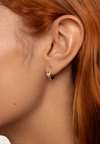 Orecchini a cerchio in tonalità oro con dettaglio in pietra gemma a forma di cuore. Design liscio e curvato che si adatta al lobo dell'orecchio. Superficie liscia e lucida.