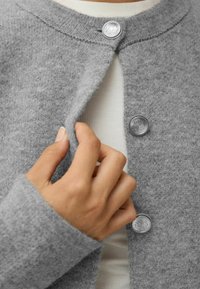 Graue Wollstrickjacke mit rundem Ausschnitt, Knopfverschluss mit dekorativen silbernen Knöpfen und weicher Textur.