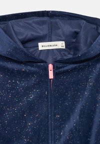Giacca con cappuccio di colore navy con accenti luccicanti, chiusura a zip con tirante rosa, materiale morbido, fodera interna e etichetta del marchio "BILLIEBLUSH."