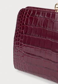 Μπορντό φουξ δερμάτινη τσάντα clutch με υφή κροκοδείλου. Διαθέτει στρογγυλή χρυσή κλείσιμο. Λείο, λαμπερό φινίρισμα.