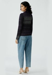 Lila und graue gestreifte Strickjacke mit hohem Kragen, kombiniert mit hellblauen weiten Jeans und beigen High-Heels.