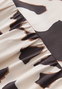 Tissu beige avec couture froncée et grand motif animalier irrégulier en brun foncé et beige.