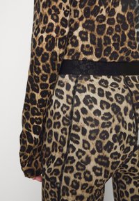 Sweter w cętki i legginsy; miękki dzianinowy materiał; ciemny pas; widoczne szwy wzdłuż szwów nóg; ogólny wzór zwierzęcy.