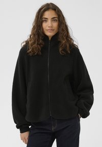 Sort fleecetrøje med høj krave, lynlåsbeslag og sidelommer; har et blødt, tekstureret stof og en løs pasform.