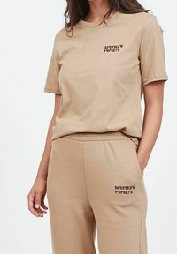 Beżowa bawełniana koszulka z krótkim rękawem, z nadrukowanymi współrzędnymi na piersi, połączona z dopasowanymi spodniami, które mają ten sam nadruk na udzie.