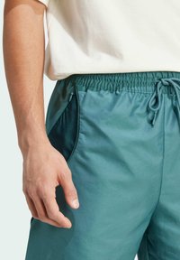 Zelené športové šortky vyrobené z ľahkého materiálu, s elastickým pásom, sťahovacou šnúrkou a bočnými vreckami s jemným leskom.