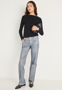 Must pikkade varrukatega tekstuuriga kangast topp, helesinised laiade säärtega teksad kahe ees oleva nupuga ning mustad teravate ninadega kingad ümmarguste dekoratsioonidega.