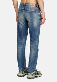 Jeans en denim bleu délavé avec une coupe slim, un design à cinq poches et une étiquette en cuir de marque à l'arrière. Portés avec des chaussures de course grises.